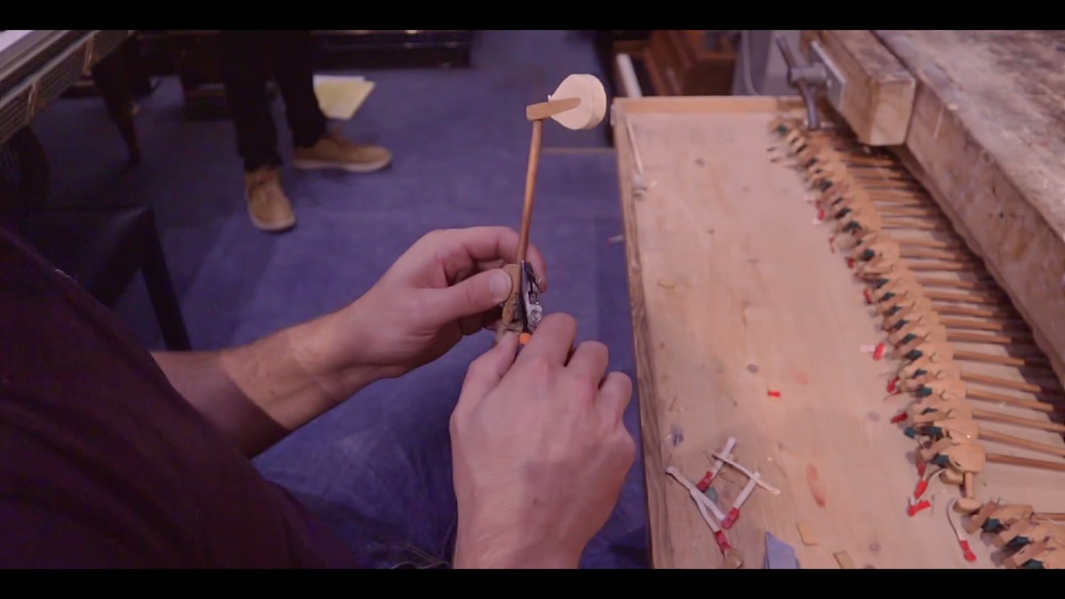 Intérieur d’un piano ouvert, avec la mécanique des marteaux et une main d’artisan intervenant délicatement sur les pièces en bois, feutre et métal.